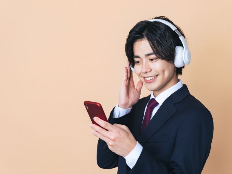 若い男性ビジネスマンがスマホとヘッドセットでリスニングの勉強をしている画像